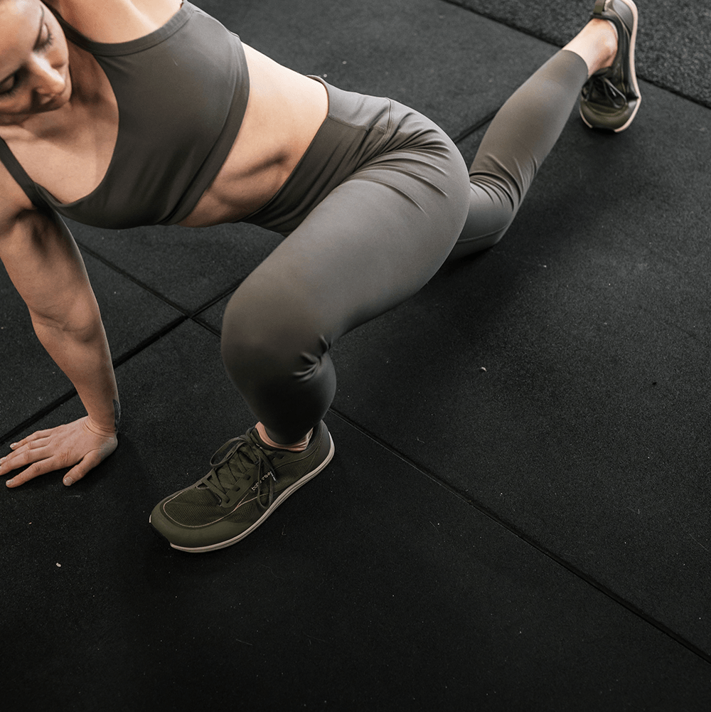 Person in athletic wear stretching on a black mat wearing Bahé shoes