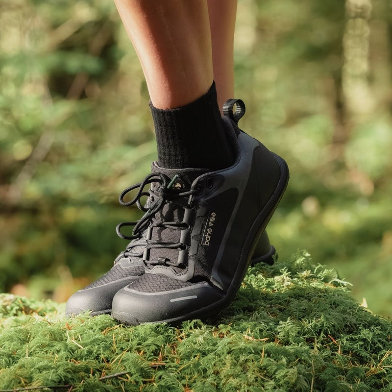 Person wearing black Bahé hiking shoes on a green forest floor