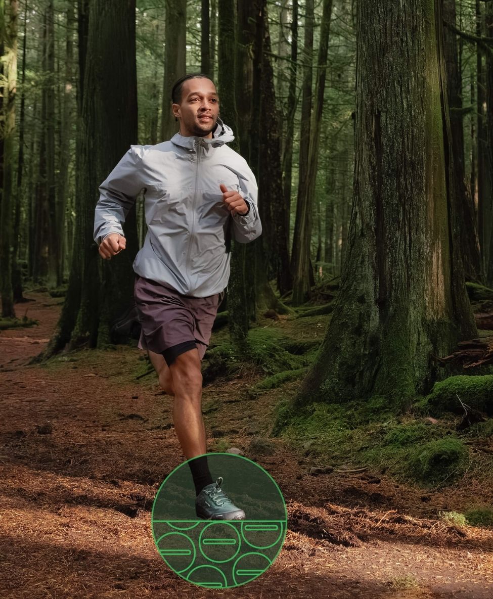 Man running through a forest wearing a Bahé grounding shoes, light jacket and shorts.