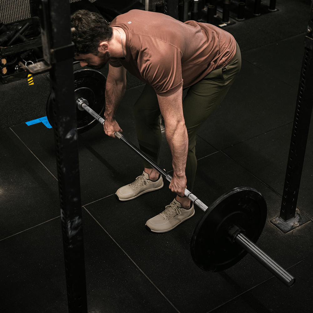 Person lifting a barbell in a gym setting wearing Bahé shoes