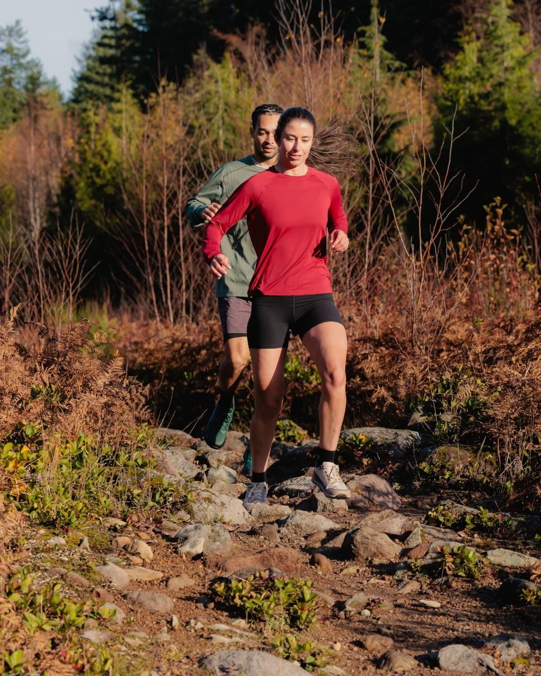 Two people running on a rocky trail in a forested area in the Rewild Shoes
