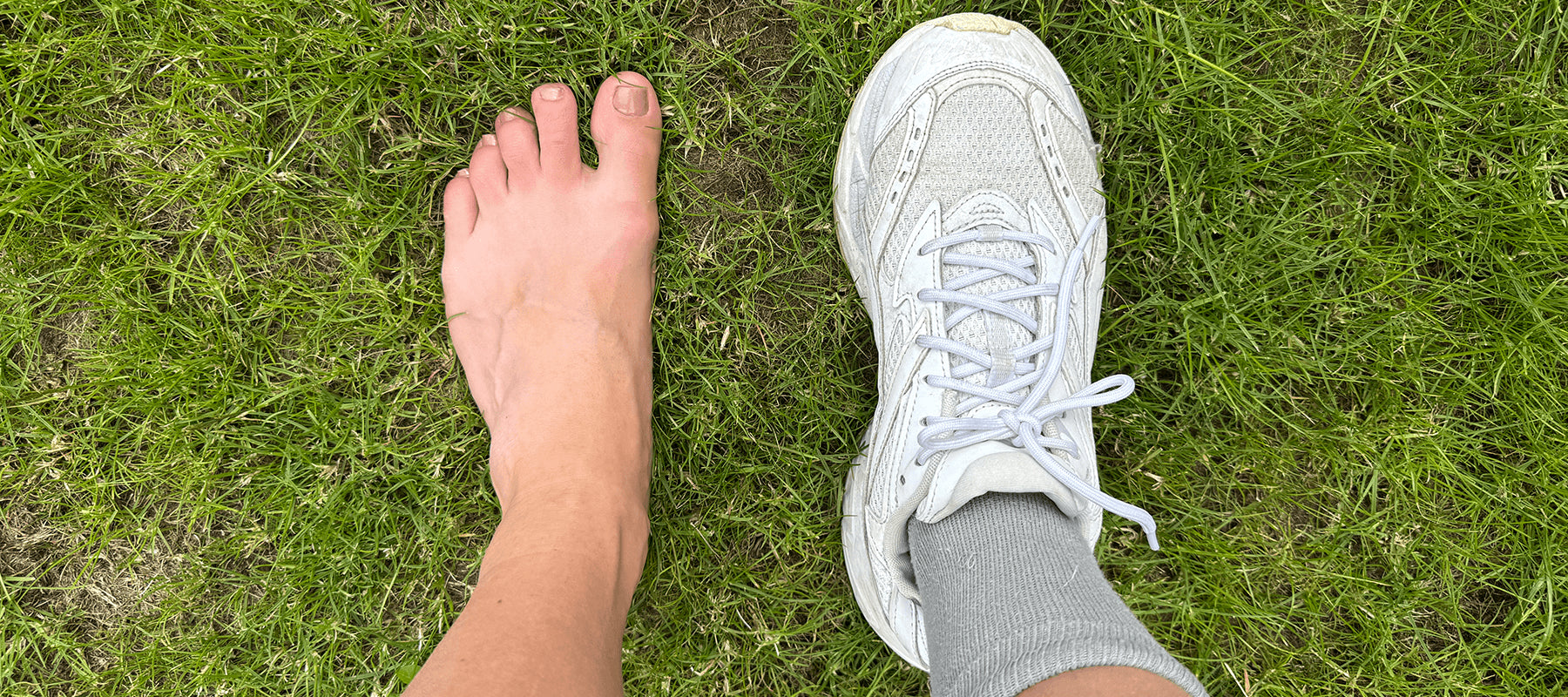 Barefoot on grass next to cushioned running shoe. 