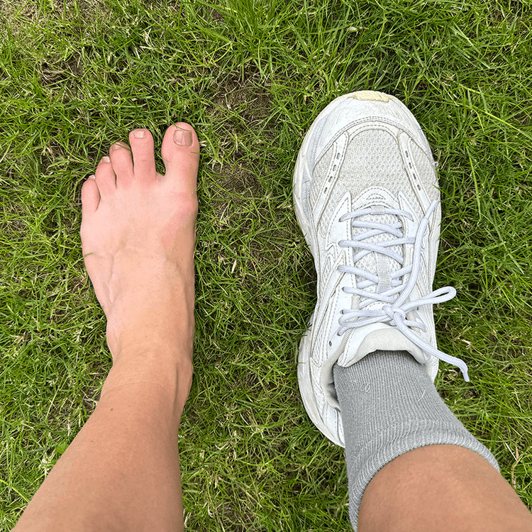 Barefoot on grass next to cushioned running shoe. 