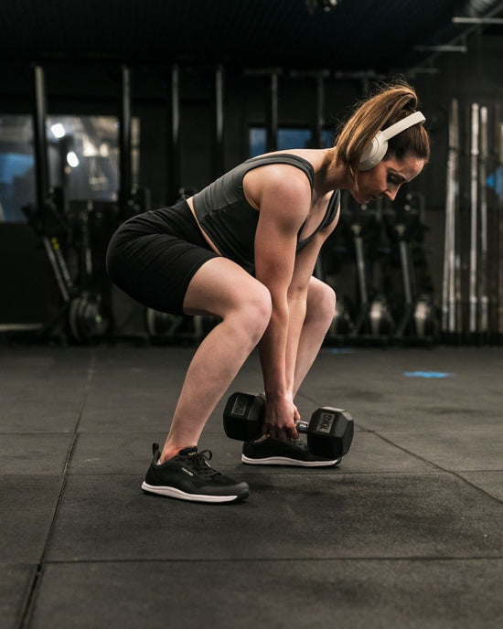 Person exercising with dumbbells in a gym setting wearing barefoot shoes