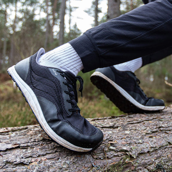 Person wearing black hiking boots with white soles on a log in a forest setting