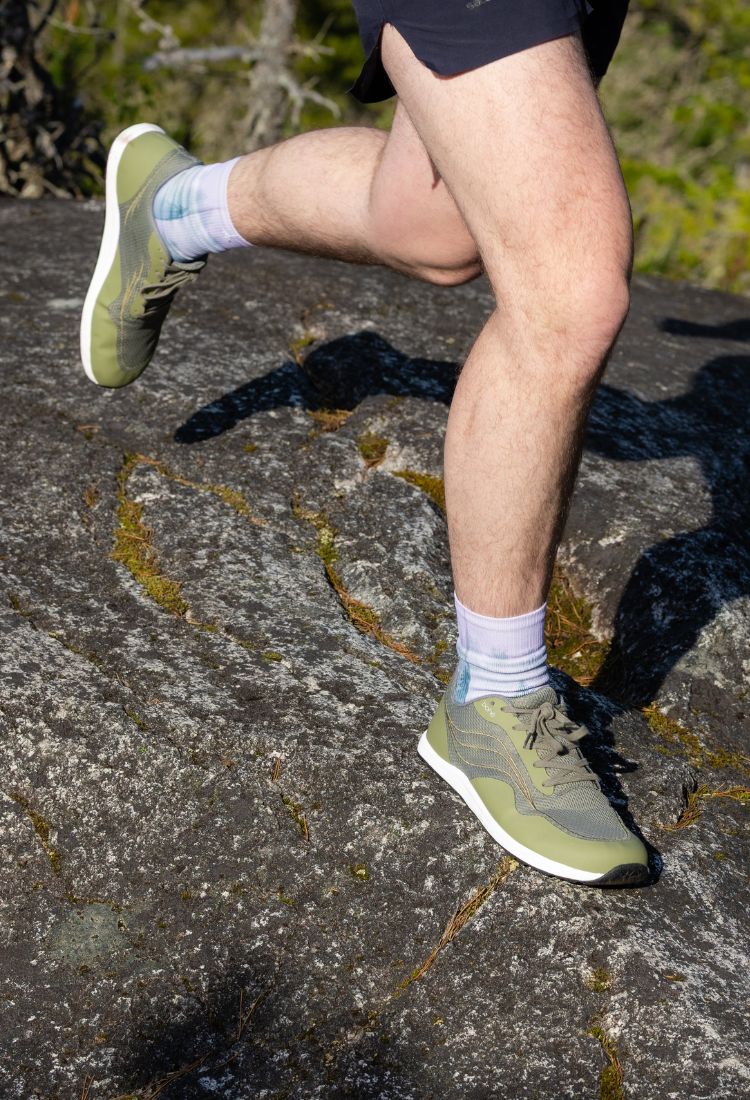 Person running on a rocky trail wearing green running shoes and white socks.