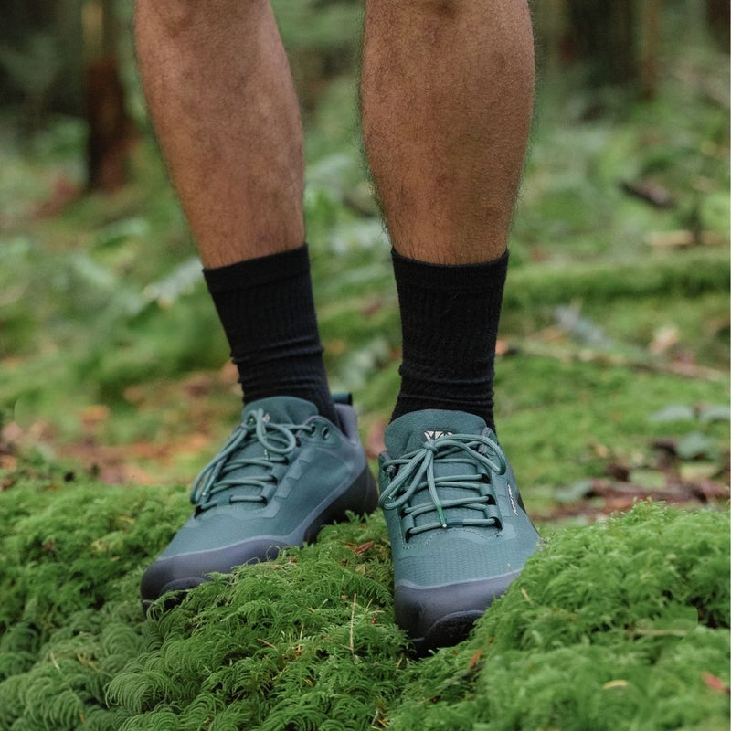 Evergreen Rewild Trail Shoes worn on a person standing on green moss with a blurred natural background