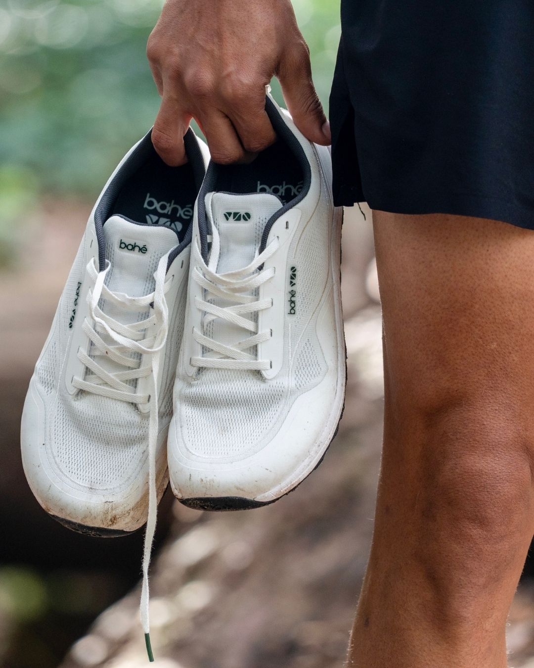 White sneakers with visible Bahé branding held by a person outdoors.