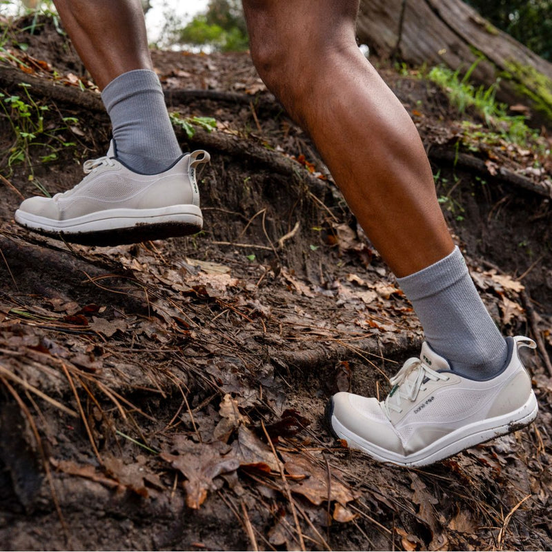 Person wearing white sneakers and gray socks walking on a forest path.