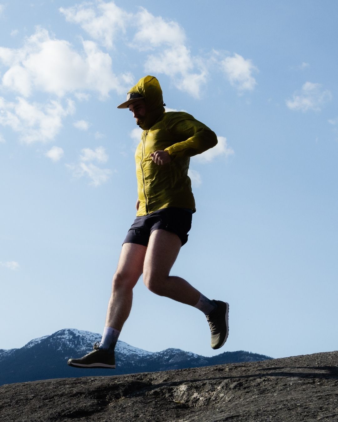 Person running on a mountain trail with a clear blue sky and mountains in the background