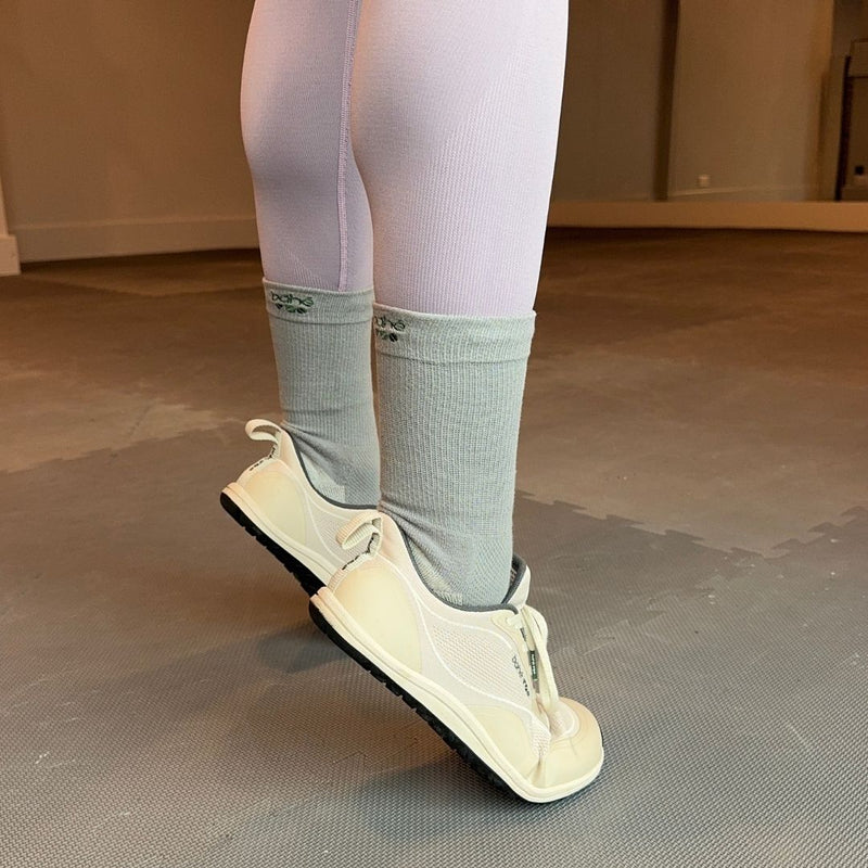 Person wearing white sneakers and light gray socks on a neutral background
