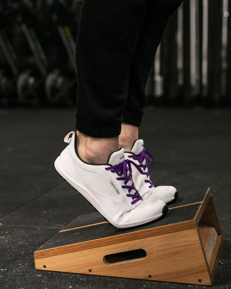 Person stepping onto a wooden box with white sneakers and purple laces.