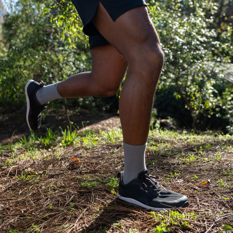 Person running on a trail with greenery in the background wearing Bahé shoes