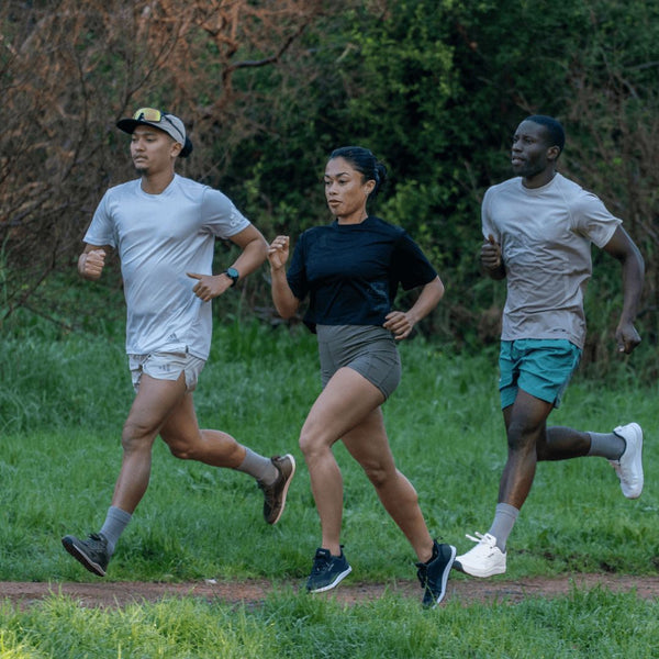 Three people running outdoors on a grassy path with trees in the background